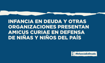 Imagen de portada con fondo azul marino y una franja irregular en beige en la parte superior que simula una ruptura. Texto en blanco: "Infancia en Deuda y otras organizaciones presentan amicus curiae en defensa de niñas y niños del país". En el ángulo inferior derecho, el logo de #InfanciaEnDeuda.