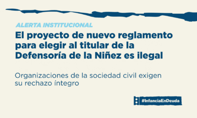 Imagen apaisada con fondo crema y franja azul oscuro rasgada en el borde superior. Volanta en celeste: "Alerta institucional". Título en azul: "El proyecto de nuevo reglamento para elegir al titular de la Defensoría de la Niñez es ilegal". Bajada: "Organizaciones de la sociedad civil exigen su rechazo íntegro". Abajo a la derecha, el logo de #InfanciaEnDeuda.